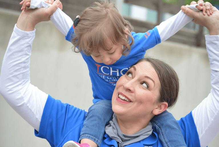 Mother with Daughter Sitting on Her Shoulders Smiling Wearing CHCP Shirts